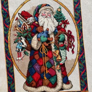 Könnte beinhalten: Ein Kreuzstichbild von Santa Claus, der Spielzeug und Geschenke hält. Er trägt einen bunten Patchwork-Mantel, einen pelzbesetzten Umhang und einen Hut. Das Bild ist mit einem goldenen Rahmen und einem grün-roten Dekorationsmuster versehen, das ein weihnachtliches Thema hervorruft.