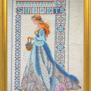 May include: Cross-stitch artwork in a gold frame. The image depicts a woman in a blue gown carrying a basket of flowers. The word "SUPERB" is stitched at the top. The artwork features intricate patterns and details.
