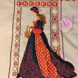 Può includere: Schema di punto croce con una donna in un abito rosso e blu che tiene un cesto di fiori. Lo schema è incorniciato da un bordo che dice "Inghilterra".