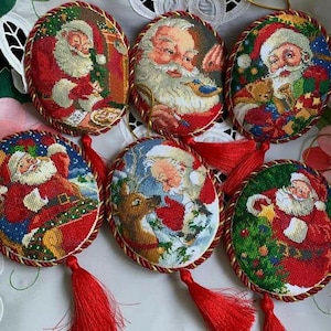 May include: Six round, red and gold Christmas ornaments with embroidered images of Santa Claus. Each ornament has a red tassel.