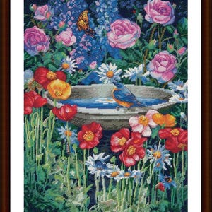 Może przedstawiać: Niebieski ptak siedzi na krawędzi kamiennej kąpieli dla ptaków otoczonej bujnym ogrodem z różowymi różami, czerwonymi makami i białymi stokrotkami.