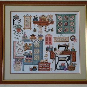 Può includere: Opera d'arte a punto croce incorniciata che raffigura una scena di cucito accogliente. L'opera presenta una macchina da cucire Singer, mensole con vari oggetti legati al cucito, una trapunta e il testo "Home Sweet Home". La tavolozza dei colori include blu, rosa e marrone.