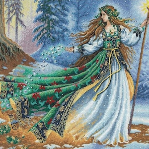 May include: A woman in a white dress with a green and gold patterned skirt and a crown of leaves on her head stands in a snowy forest. She is holding a staff with a star on top and is scattering sparkling dust from her hand.