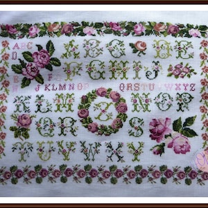 May include: Cross-stitch sampler featuring an alphabet with floral embellishments. The design includes pink roses, green leaves, and decorative borders. The letters are in various styles, with a central wreath.