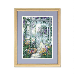 May include: Cross-stitch artwork of a garden scene framed in a light wood frame. The scene depicts a stone path leading to a white gate, surrounded by colorful flowers, a basket of blooms, and climbing vines. The artwork is set against a light blue background.