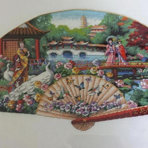 May include: A colourful embroidered fan depicting a traditional Chinese garden scene with peacocks, flowers, and figures in ornate clothing. The fan is framed with a gold trim and has a red and gold handle.