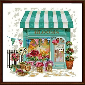 May include: A green storefront with a white awning and the word "BLOOMS" in white letters. The shop window displays a variety of colorful flowers and the word "Flowers" in a white sign. There are baskets of flowers outside the shop.