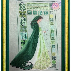 Può includere: Un ricamo a punto croce di una donna con un vestito e un mantello verdi, in piedi in un bordo di nodi celtici verdi e bianchi. Il ricamo è incorniciato da una cornice dorata e verde.