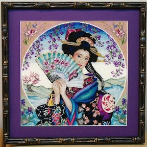 Può includere: Un ricamo a punto croce di una donna in un tradizionale kimono giapponese che tiene un ventaglio. La donna ha lunghi capelli neri e indossa un kimono colorato con motivi floreali. Lo sfondo è rosa e blu tenue con una cornice circolare di fiori di glicine.
