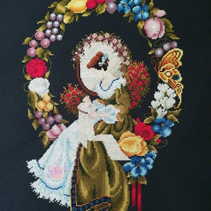 Könnte beinhalten: Eine Kreuzstich-Stickerei, die eine Frau in einem weißen Kleid und einer grünen Jacke zeigt, die in einem Kranz aus Blumen und Früchten sitzt. Der Kranz besteht aus roten, gelben und blauen Blumen, grünen Blättern und lila Trauben. Ein Schmetterling fliegt über dem Kranz.