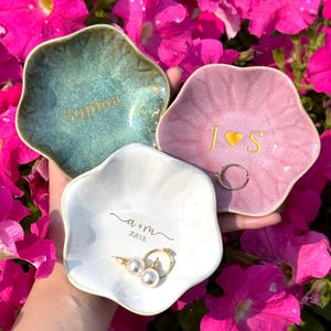 May include: Three ceramic ring dishes in shades of teal, pink, and white, each with a unique design. The teal dish has the name "Sophia" in gold lettering. The pink dish features the initials "J ❤️ S". The white dish has the initials "a + m" and the date "2.26.18".