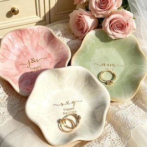 May include: Three ceramic ring dishes in pink, green, and white, each with a floral shape. The pink dish has a marble effect and the text "J&c Engaged May 20, 2026". The green dish has the text "a+m 2026.5.18". The white dish has the text "s&g Engaged Sep 21 2026".