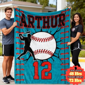 Puede incluir: Una manta turquesa con temática de béisbol con el nombre "ARTHUR" en letras negras grandes. Se presenta un gráfico de béisbol con costuras rojas y una silueta de bateador. El número "12" es rojo.