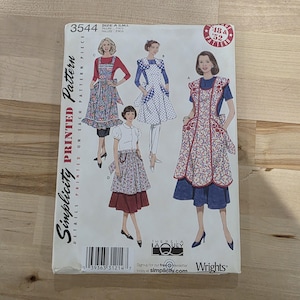 May include: A vintage Simplicity printed pattern, size A, S, M, and L. The pattern features illustrations of aprons with floral and polka dot designs. The pattern includes the text "DETAILS PRINTED ON EACH PATTERN PIECE".