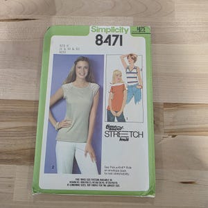 May include: A Simplicity 8471 sewing pattern for Misses sizes 8, 10, and 12. The pattern features a woman wearing a knit top and white pants. The pattern includes the text "time saver STRETCH knit".