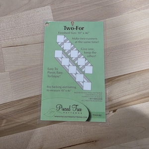 May include: A green and white Two-For pattern for making two quilt runners, each measuring 25.4 cm x 116.8 cm. The package includes instructions and a diagram. The text on the package says "Easy To Piece, Easy To Enjoy!"