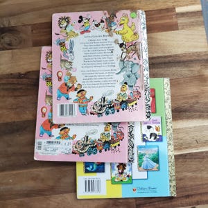 Puede incluir: Tres libros vintage de Little Golden Books con portadas rosa, azul y verde. Los libros presentan ilustraciones de un tren, un gato y una princesa. La contraportada del libro rosa tiene texto que dice "Little Golden Books" y "A los niños les han encantado los Little Golden Books durante más de 50 años."