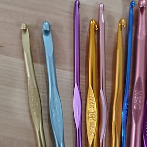 May include: A set of nine crochet hooks in various colors, including gold, purple, pink, blue, and silver. The hooks are made in the USA and have different sizes, including sizes G, H, and I.