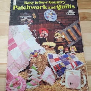 Può includere: Una copertina di libro vintage intitolata "Easy to Sew Country Patchwork and Quilts" con vari esempi di patchwork e trapunte. La copertina presenta una varietà di oggetti fatti a mano, tra cui una trapunta, un cuscino e una borsa tote con un design a mela. Lo sfondo è una scena rustica.