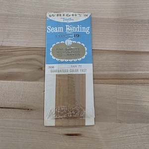 Könnte beinhalten: Eine Packung Wright's Trimtex Nahtband in der Farbe Tan 73. Die blau-weiße Verpackung enthält die Aufschriften 3 yards, fine quality woven edge, 100% rayon und guaranteed color fast. Das beigefarbene Viskoseband ist durch die Klarsichtfolie sichtbar.