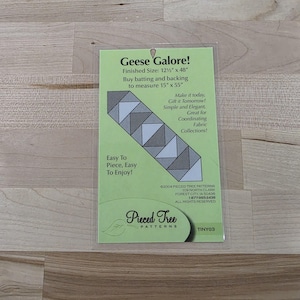 May include: A green card with the text "Geese Galore!" and a diagram of a quilt pattern. The finished size is 12.5" x 48". The card also includes the text "Easy To Piece, Easy To Enjoy!"
