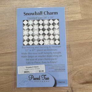 May include: A blue card in a plastic sleeve features the text "Snowball Charm" and a geometric quilt pattern. The finished size is 28" x 39". The card also includes instructions and the "Pieced Tree Patterns" logo.