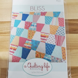May include: A quilting pattern titled "Bliss" by "a quilting life DESIGNS" by Sherri McConnell. The pattern features a colorful patchwork quilt design with a variety of fabrics in shades of blue, pink, yellow, and white.