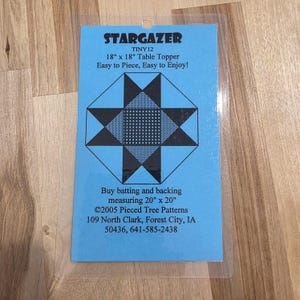 May include: A blue card with the text "STARGAZER TINY12 18" x 18" Table Topper". The card features a geometric star design in black and white. The text "Easy to Piece, Easy to Enjoy!" is also visible.