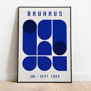 May include: A black and white poster with the text "BAUHAUS" in bold, blue letters. The poster features a geometric design of blue circles and semi-circles. The text "JUL - SEPT 1923" is at the bottom of the poster.