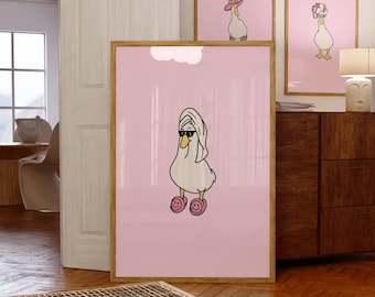 May include: Three framed art prints featuring cartoon geese on a pink background. The main print shows a goose wearing sunglasses, a towel, and slippers. The other prints show geese wearing hats. All prints have a wooden frame.