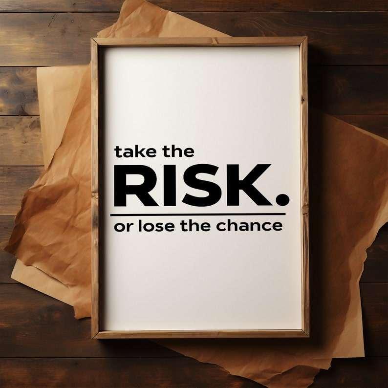 Peut inclure: Une affiche motivationnelle encadr&eacute;e avec un fond blanc et du texte noir qui dit "take the RISK. or lose the chance". L'affiche est pos&eacute;e sur une surface en bois brun.