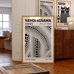 May include: Three framed art prints featuring Yayoi Kusama artwork. The prints have a wooden frame and display black and white polka dot patterns and Japanese text. One print shows two black cats with polka dots. The text "YAYOI KUSAMA" is visible.