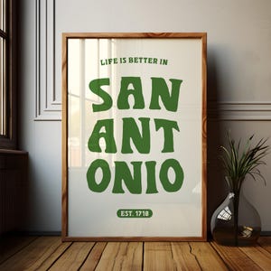 Puede incluir: Una impresi&oacute;n enmarcada con fondo blanco y texto verde que dice "Life is better in San Antonio. Est. 1718".