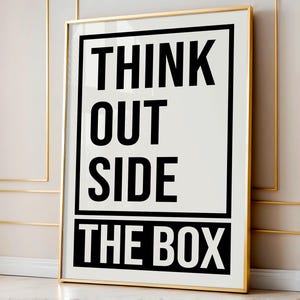 Puede incluir: Un p&oacute;ster motivacional en blanco y negro con marco dorado. El p&oacute;ster dice "Think Outside The Box".