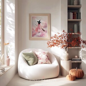 May include: A cozy living room scene featuring a framed artwork of a witch in a pink dress flying on a broom. A white beanbag chair with green and floral pillows sits below the artwork. Pumpkins and fall foliage add seasonal decor.