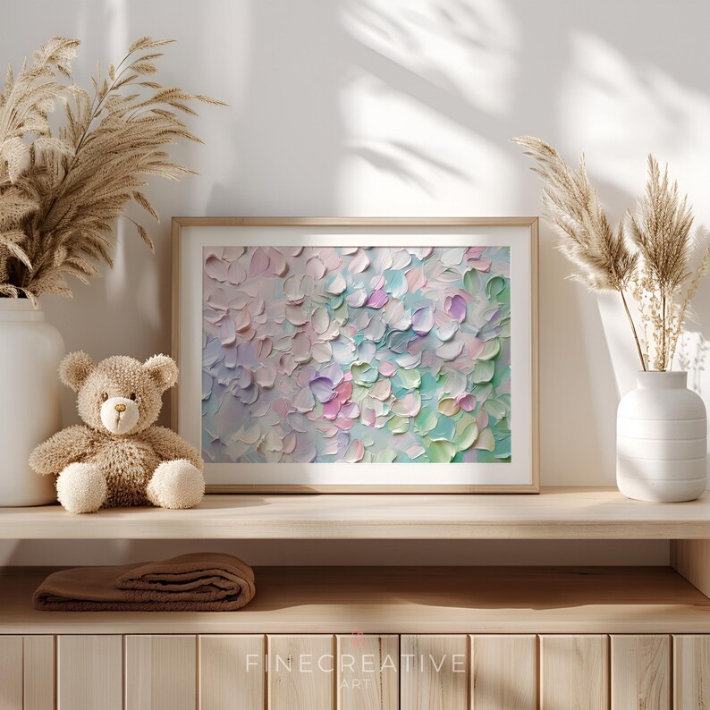 Op de afbeelding: Een ingelijst abstract schilderij met een textuur in impastostijl. Het kunstwerk heeft een palet van zachte roze, blauwe, groene en paarse tinten. Het schilderij wordt tentoongesteld op een houten plank met een teddybeer, vaas en decoratieve droge planten.