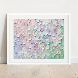 Op de afbeelding: Ingelijste abstracte bloemenkunstprint. Het kunstwerk heeft een textuur in impastostijl met een palet van zachte pastelkleuren, waaronder roze, lavendel, groen en wit. Het schilderij is geplaatst in een witte lijst en wordt getoond op een lichte houten vloer.