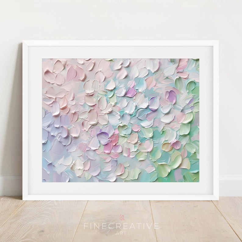 Op de afbeelding: Ingelijste abstracte bloemenkunstprint. Het kunstwerk heeft een textuur in impastostijl met een palet van zachte pastelkleuren, waaronder roze, lavendel, groen en wit. Het schilderij is geplaatst in een witte lijst en wordt getoond op een lichte houten vloer.