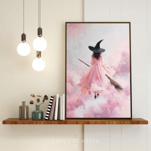 May include: A framed art print depicts a witch in a pink dress and black hat flying on a broom through a pink and white cloudy sky. The artwork is displayed on a wooden shelf with decorative items.