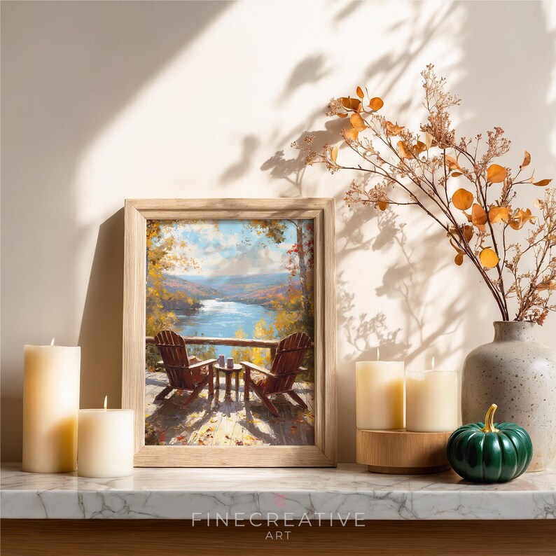 May include: A framed landscape painting depicts two wooden Adirondack chairs on a deck overlooking a lake. The painting is surrounded by candles, a decorative vase with branches, and a small green pumpkin.