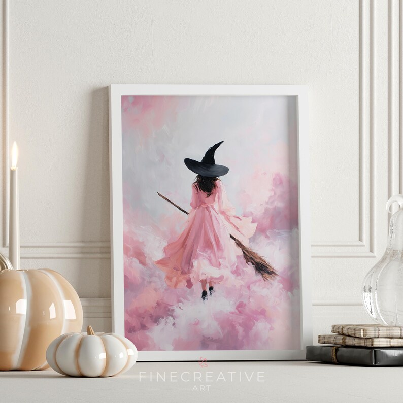 May include: A framed art print featuring a witch in a pink dress and black hat flying on a broomstick through a pink and white cloudy sky. The artwork is signed "Fine Creative Art" at the bottom.