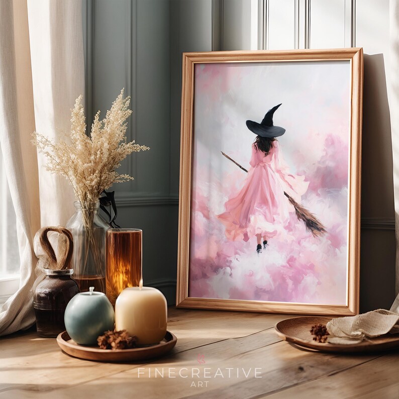 May include: A framed art print depicts a witch in a pink dress flying on a broom through pink clouds. The artwork is in a wooden frame and is displayed on a wooden table. The text "FINECREATIVE ART" is at the bottom.