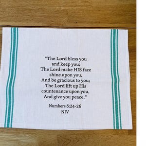 May include: White kitchen towel with teal stripes on the edges. The towel features the text of Numbers 6:24-26, a biblical verse, in black font. The NIV version of the verse is also noted.