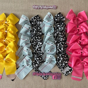 Może przedstawiać: Zestaw 30 kokardek do włosów w szkolnym stylu. Kokardki są żółte w czarne paski, niebieskie w czarne i białe kropki oraz różowe z napisem "Pink Eraser".