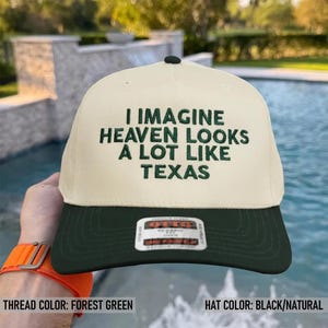 May include: A black and natural-colored baseball cap with the embroidered text "I IMAGINE HEAVEN LOOKS A LOT LIKE TEXAS" in forest green. The hat has a curved brim and a button on top.