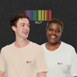 Könnte beinhalten: Zwei Personen tragen T-Shirts mit einem Regenbogen-Barcode-Design und dem darunter gedruckten Wort "ALLY". Der Barcode ist ein Symbol der Unterstützung für die LGBTQ+-Community.