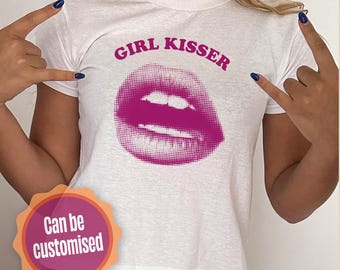 Puede incluir: Camiseta blanca con un gráfico de labios rosas y el texto "GIRL KISSER" en letras rosas.