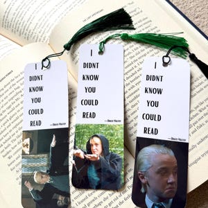 May include: Three rectangular paper bookmarks with green tassels, each featuring the text I DIDNT KNOW YOU COULD READ and a quote attribution to Draco Malfoy. The bookmarks display different photographic images of a person with blonde hair.