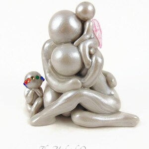 May include: A silver-colored sculpture depicting a family of four. The figures are stylized with rounded forms, with one child wearing a colorful beaded headband and another with pink wings. The Midnight Orange logo is at the bottom.