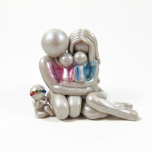 May include: A pearlescent figurine depicting a family of five. The parents embrace two children, with the youngest child seated nearby. The children have pink and blue accents. The youngest child wears a colorful jeweled headband.